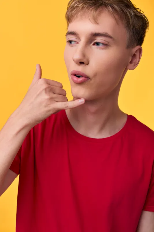Hand gesture signaling call me by a young man in a red shirt against a bright yellow backdrop, showcasing clear communication and casual studio style for marketing and social media