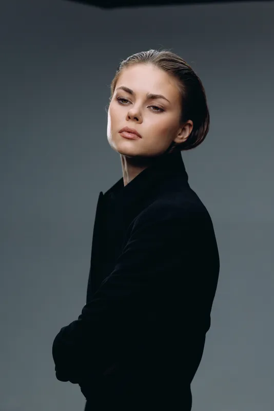 Portrait of serious woman in black clothing with folded arms on gray background