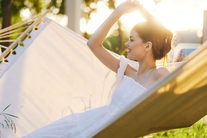 Young woman in a white dress relaxing in a hammock during sunset, exuding tranquility and joy in a vibrant summer setting