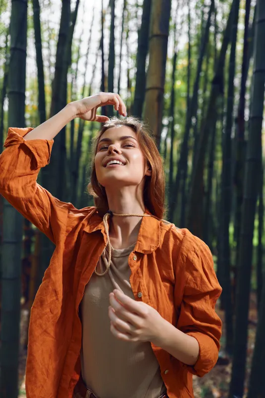 Woman bamboo forest portrait in nature outdoors with smile and relaxed fashion style, young female enjoying sunlight between tall bamboo stalks for serene eco lifestyle mood.