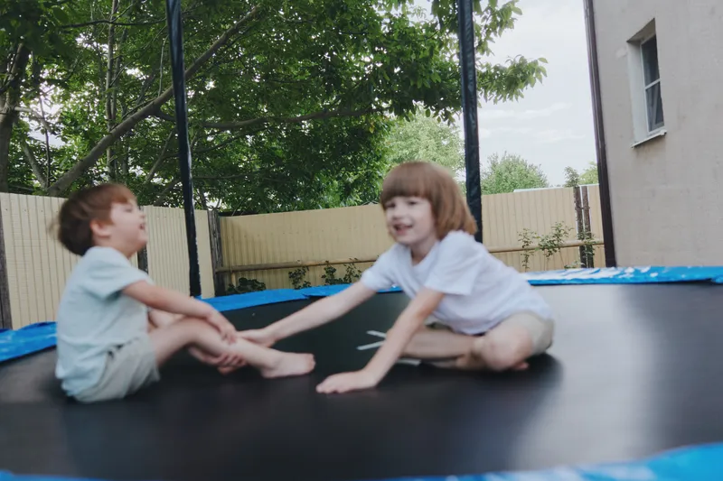 Happy children playing on a trampoline in a sunny garden, enjoying the outdoors and having fun together. Laughter and joy fill the atmosphere.