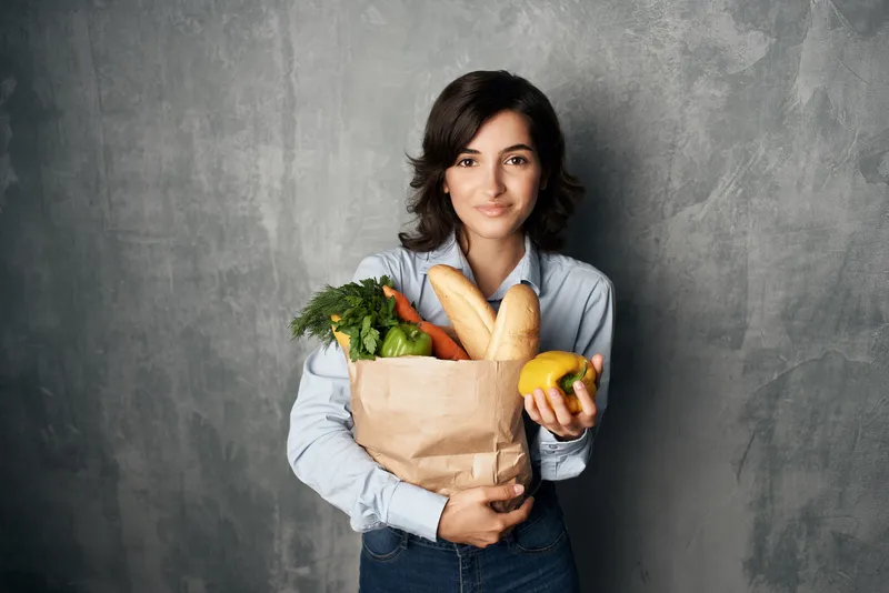Женщина с пакетом продуктов, овощами, здоровой пищей, снятая в студии на фоне супермаркета