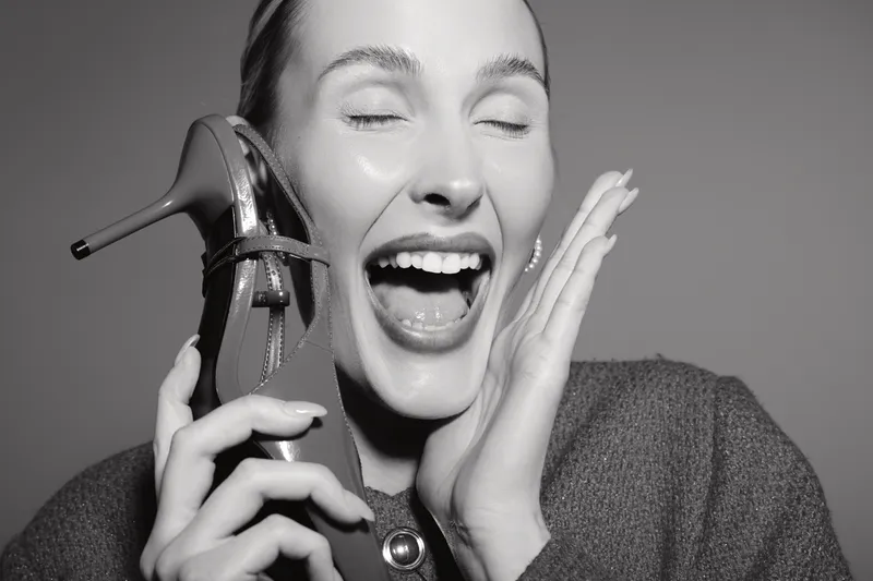 Happy white woman with fair skin holds high heel shoe near face, eyes closed and smiling. Concept for fashion, footwear, joy and beauty.