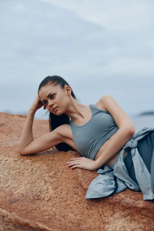 Young woman in activewear poses gracefully on a rocky surface while enjoying the serene backdrop of nature, reflecting a calm and confident demeanor
