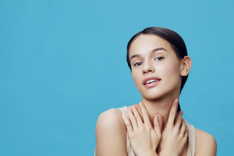 Young woman with a fresh look, showcasing natural beauty against a blue background, expressing confidence and serenity, perfect for beauty and wellness themes
