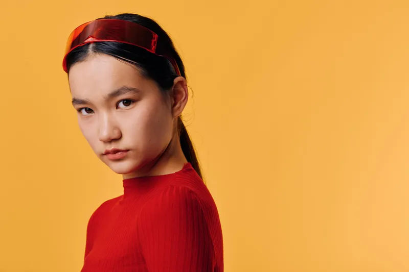 Young woman with red headband and red top posing with serious expression on orange background. Portrait, fashion style and confident female model in studio with clean backdrop.