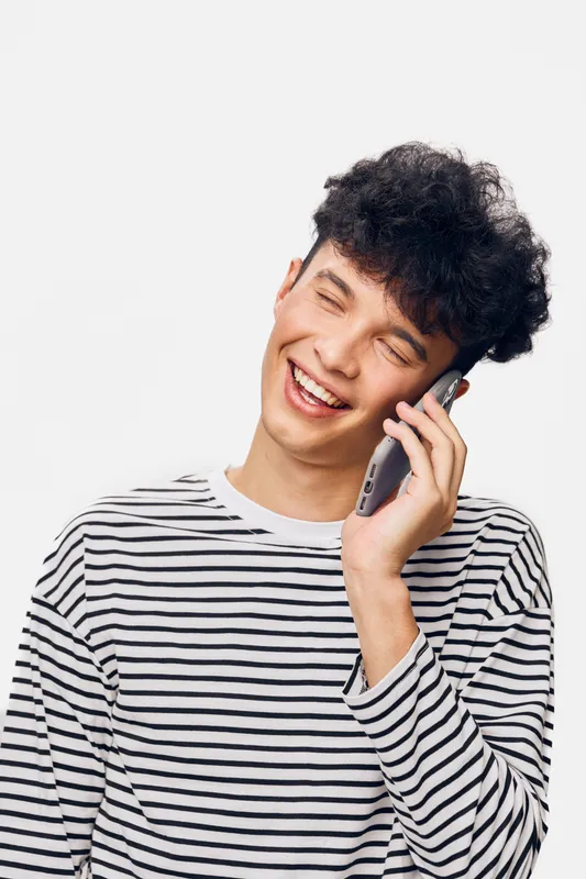 smiling man talking on phone wearing striped shirt against white background, casual style, joyful expression, communication concept