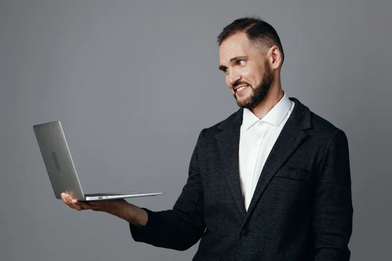 Professional man presents a laptop with a confident smile against an isolated colored background, conveying focus, leadership, and positive emotion in a modern business setting.
