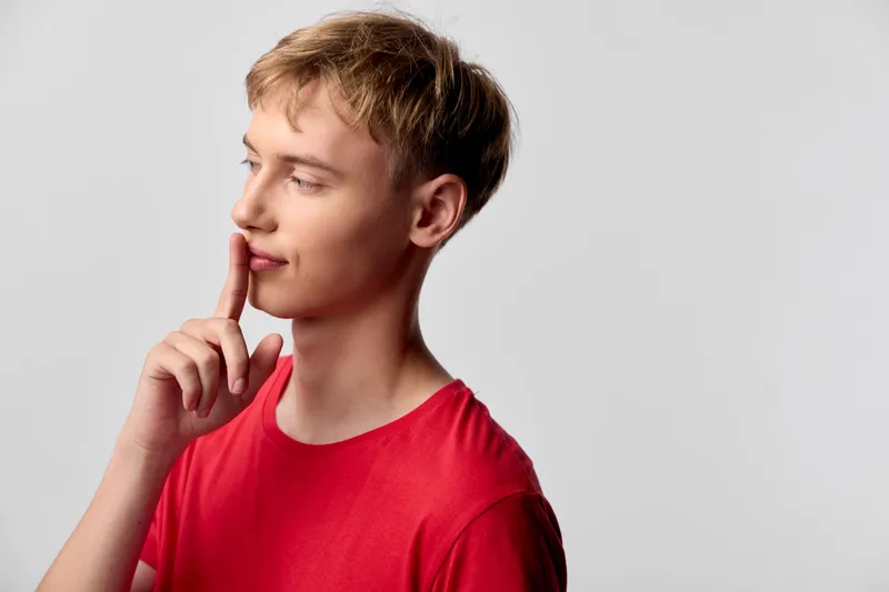 Thinking, finger on lips, red shirt, studio setting captures contemplation and curiosity, a quiet thoughtful mood suitable for education, creativity and communication themed projects