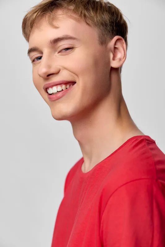 Smile, young man, red shirt, casual headshot with cheerful expression and friendly energy, bright lighting, simple background, positive vibe and approachable confidence