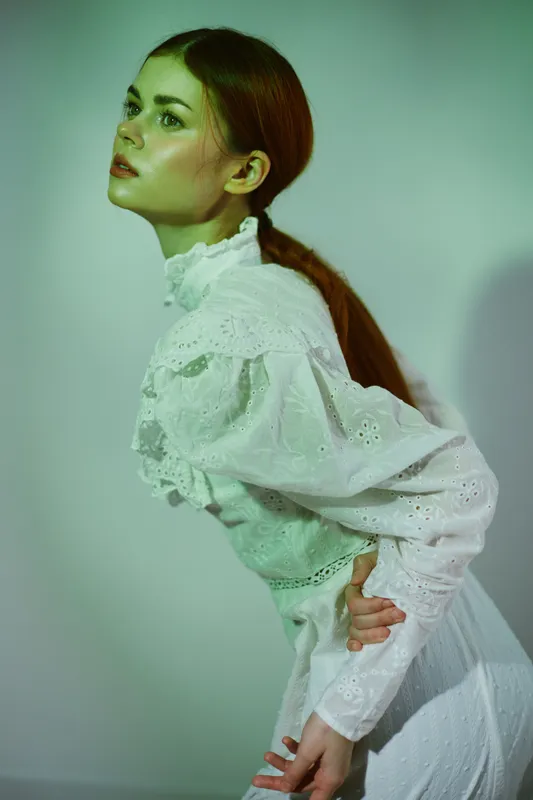 Elegant model with long red hair in a vintage white blouse against a green toned background, expressing serene beauty and calmness in a minimalist style