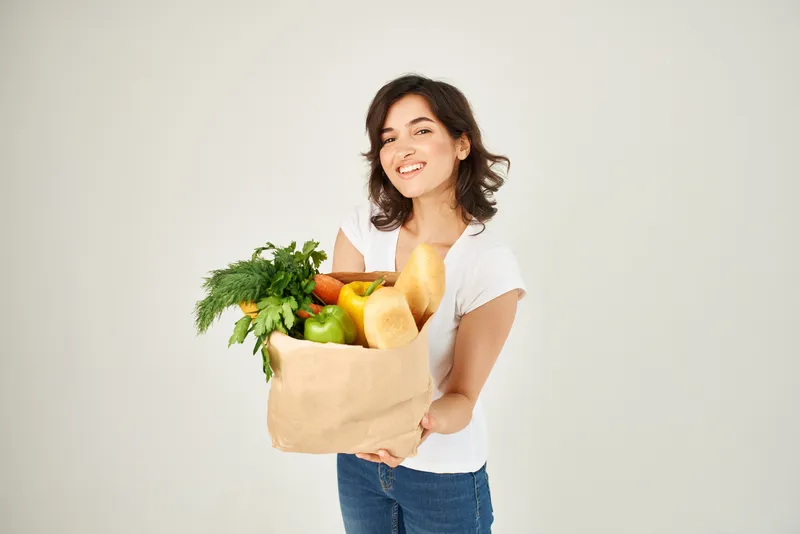Весёлая брюнетка с бумажным пакетом продуктов и овощей