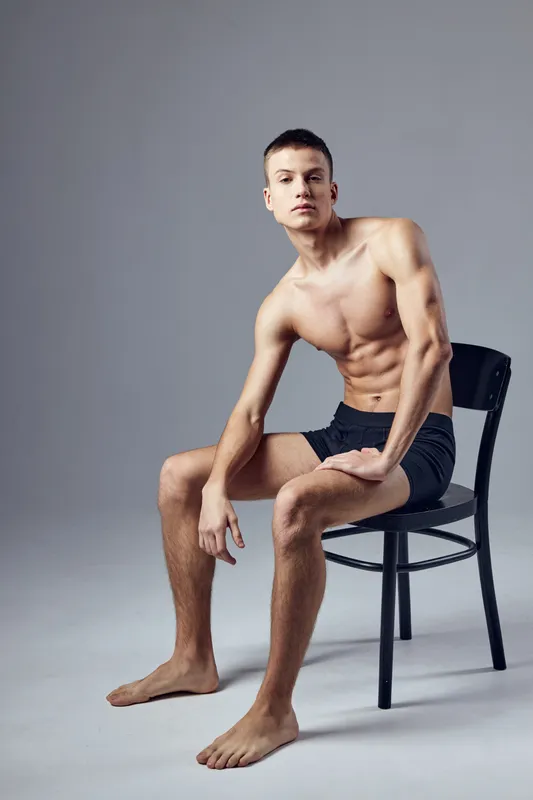 Спортивный мужчина с накачанным мускулистым телом сидит на стуле на изолированном фоне