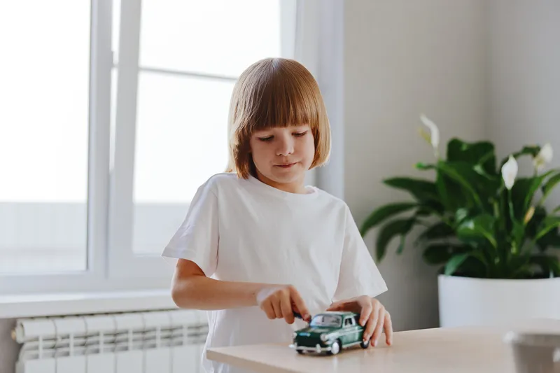 Engaged boy playing with a toy car in a bright room filled with greenery, showcasing a joyful moment of childhood innocence and imagination.