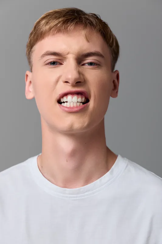 Closeup of an angry young man grimacing, displaying teeth and tense facial muscles to convey frustration, intensity, and bold emotion in a dramatic moment