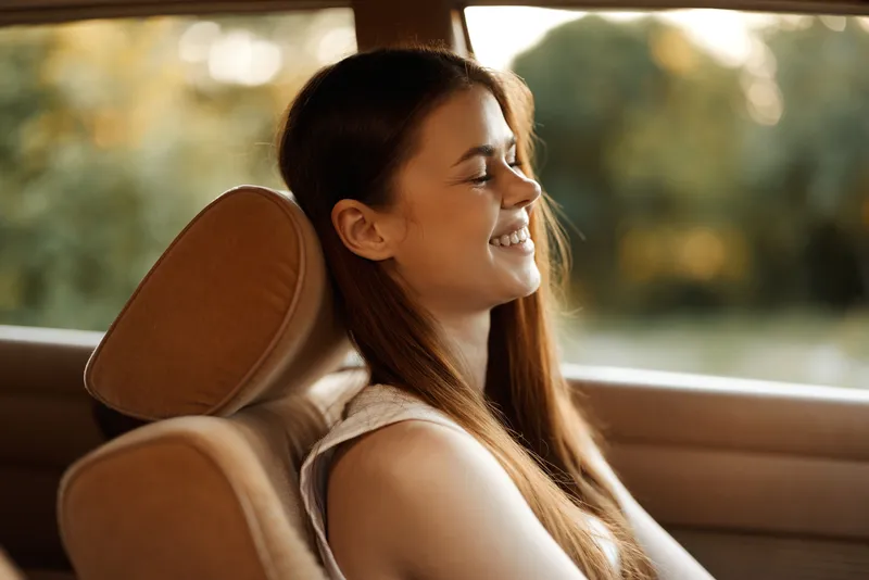 Young woman enjoying a serene moment in a car with a relaxed expression, captured in warm natural light amidst greenery.