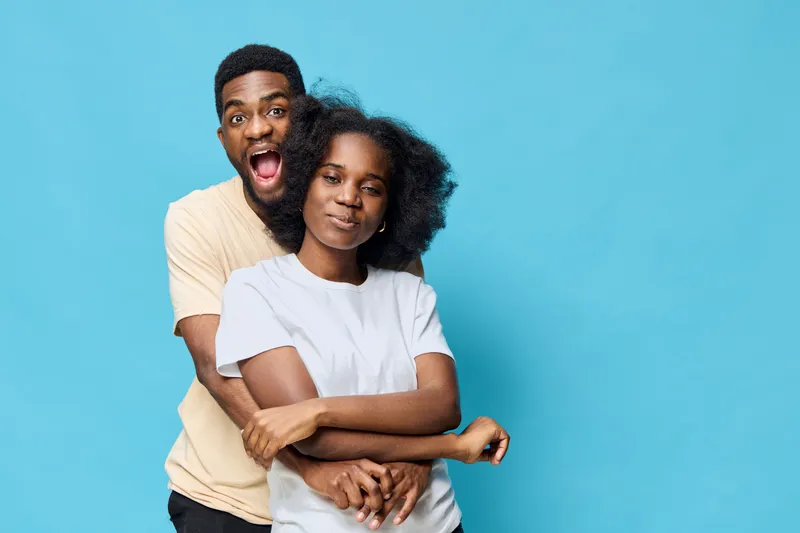 Happy young African couple embracing each other against a vibrant blue background, showcasing joy and love through their expressions and casual wear
