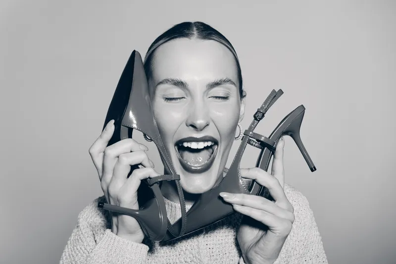 Happy Caucasian woman with fair skin holds two high heel shoes near face with closed eyes and open mouth. Concept of fashion, joy, and female excitement.