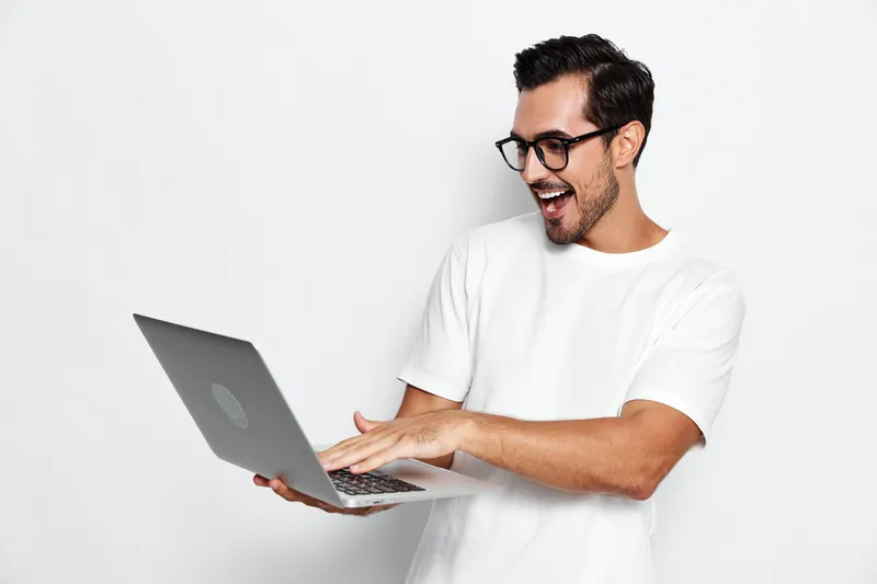 Happy excited man using laptop while smiling and looking at the camera with a joyful expression isolated on plain solid white background. Lifestyle concept.
