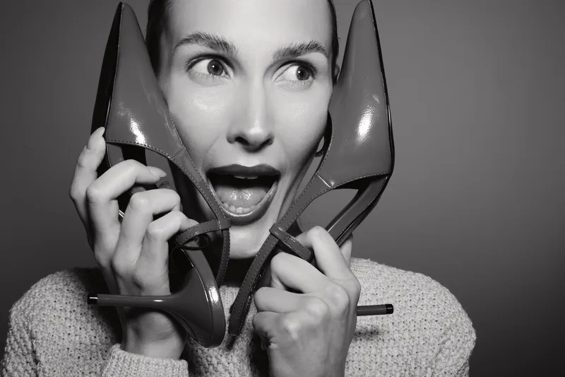 Excited Caucasian woman with light skin holds red high heels near her face. Concept for fashion, shoes, style, and shopping joy in studio black and white photo.