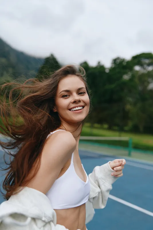 Smiling young woman in sportswear enjoying an outdoor workout in nature, demonstrating fitness and happiness on a cloudy day