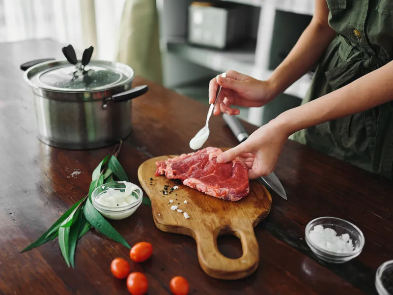 Женщина на кухне готовит ужин из мяса, овощей и специй на деревянном столе на фоне стильной кухни, крупным планом руки, свежие экопродукты, образ жизни
