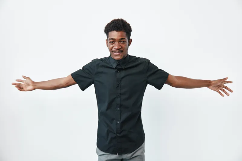 African man with dark skin wearing black shirt standing with arms wide open smiling on white background. Young adult male, casual clothing and positive expression.