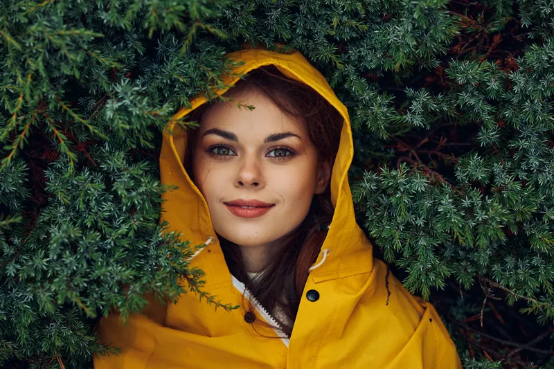 Женщина в жёлтом дождевике, окружённая зелёными деревьями и кустарниками в красивом лесном массиве