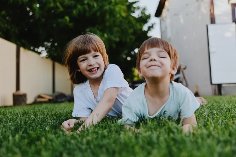 Joyful children playing on the grass, smiling and enjoying their summer day in the backyard. Bright sunshine and cheerful atmosphere enhance their happiness.