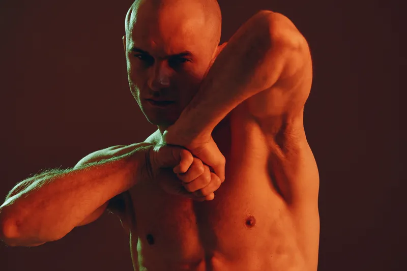Muscular man demonstrating strength and determination, showcasing impressive physique and focused expression against a dynamic background.