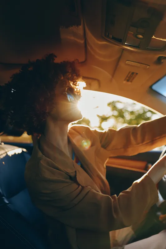 A woman lifestyle driving car in sunlight with retro film color, conveying a warm candid moment of movement and travel, a casual, focused mood in everyday driving.