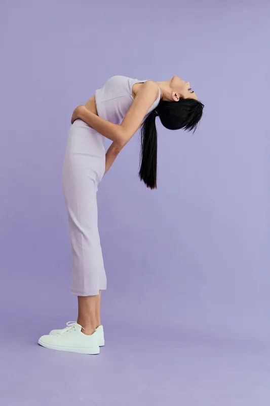 woman stretching backward in white dress and sneakers on purple background, demonstrating flexibility and balance in modern minimalist style