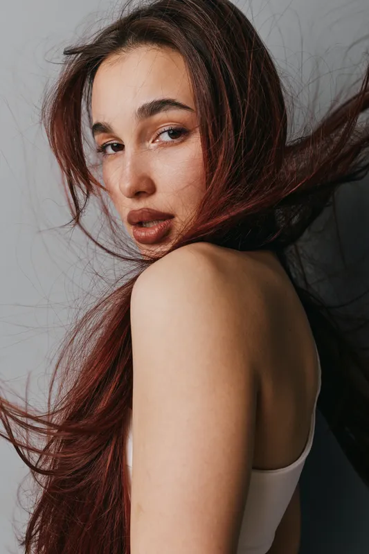 Portrait of young woman with long hair looking over shoulder against neutral background. Beauty, fashion and natural makeup with casual style and confident expression in studio.