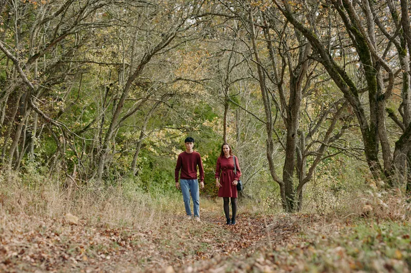 A candid, authentic portrait of a couple walking hand in hand along a quiet autumn woodland path, conveying genuine connection, natural expressions and a simple outdoor lifestyle.