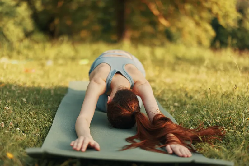 Young woman practicing yoga outdoors in a serene green park setting, wearing a comfortable outfit, promoting wellness and mindfulness through yoga and nature