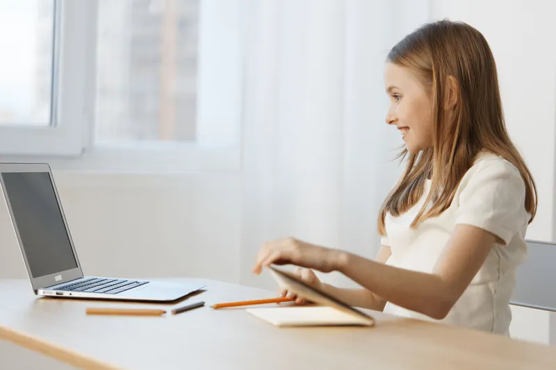 Young girl studying at a desk using a laptop, smiling with excitement Bright, light background enhances the learning atmosphere and youthful energy