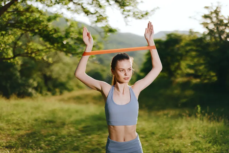 Young athletic woman exercising outdoors with a resistance band, showcasing determination and strength in a natural green setting