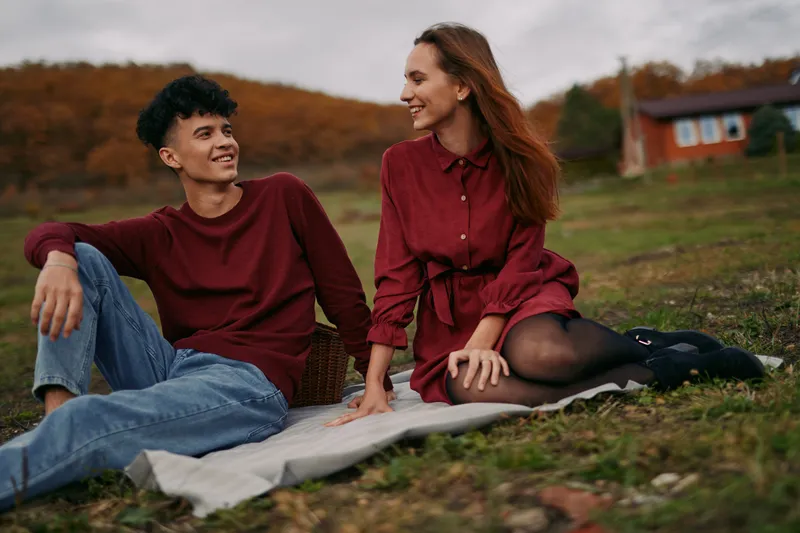 A candid portrait of a young couple sharing a genuine outdoor picnic moment, conveying authenticity and credibility through relaxed body language, warm eye contact and natural smiles.