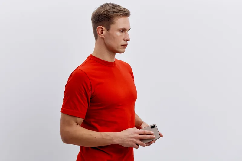 serious caucasian man wearing red t-shirt holding smartphone looking aside isolated on white background digital nomad lifestyle technology concept