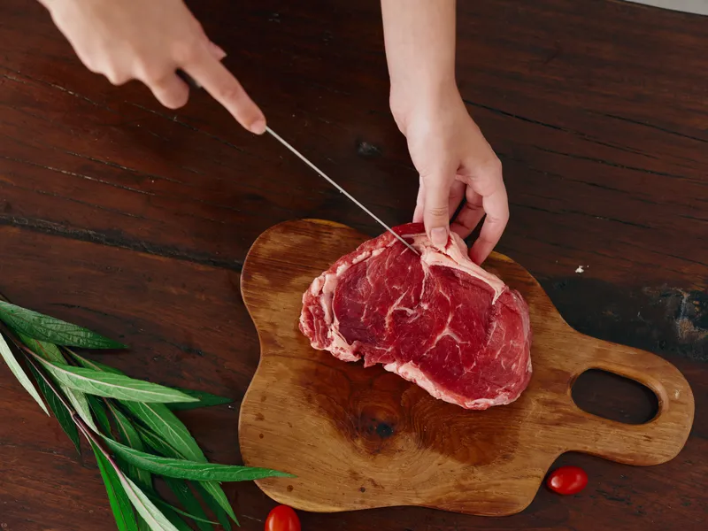 Женщина с ножом в руке нарезает свежее мясо для стейка, которое будет запекаться на кухне