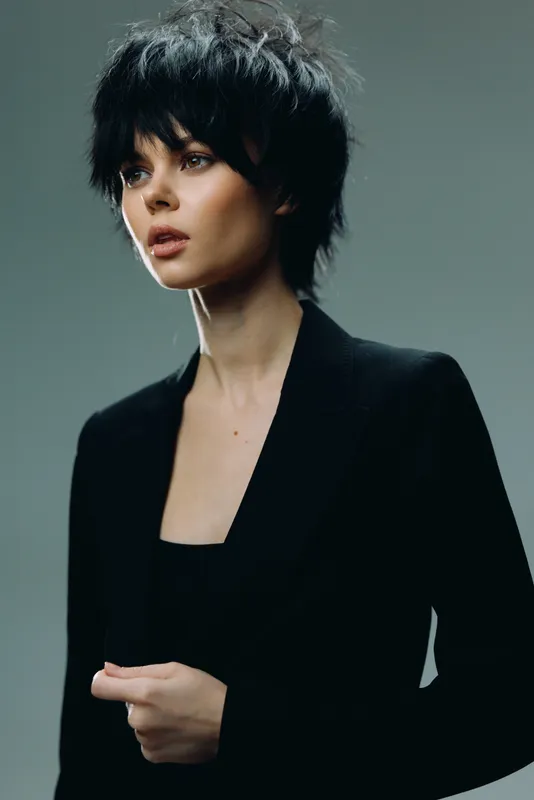 Young woman with short black hair wearing a black blazer looking thoughtfully with soft lighting
