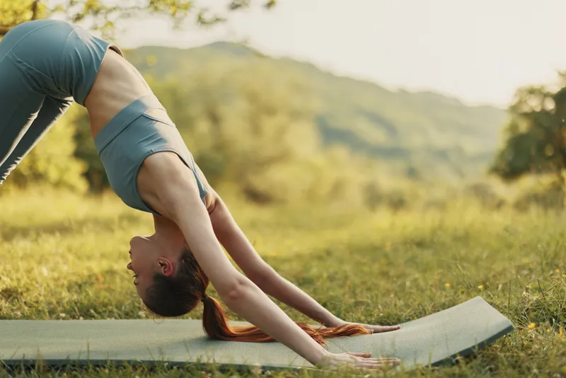 A flexible young woman practicing yoga outdoors in a serene, natural setting with a beautiful green background, embodying tranquility and balance