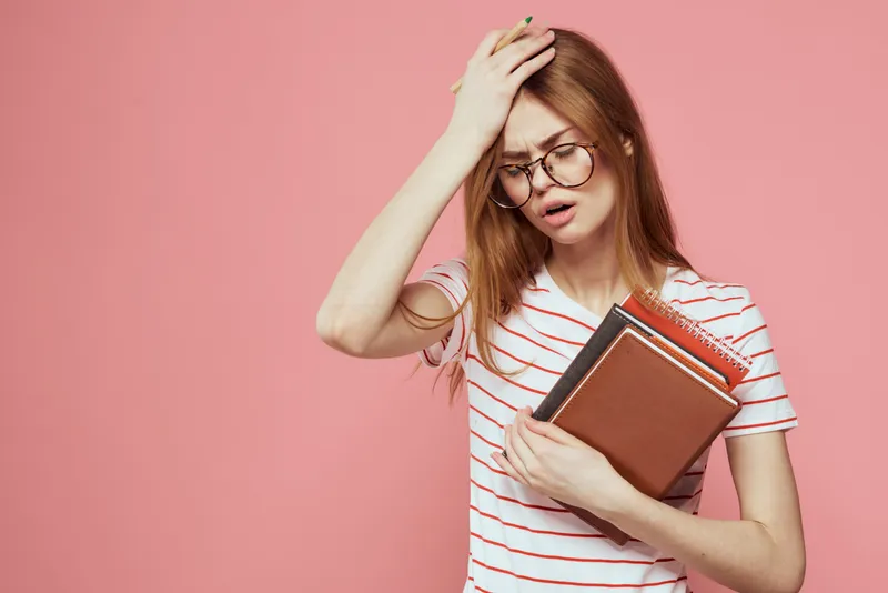 Молодая студентка с книгами на розовом фоне, в очках на лице, кадрированный вид, учебное заведение