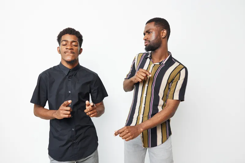 Two joyful African American men engaging in a lively dance, showcasing their stylish outfits and vibrant emotions against a clean white background.