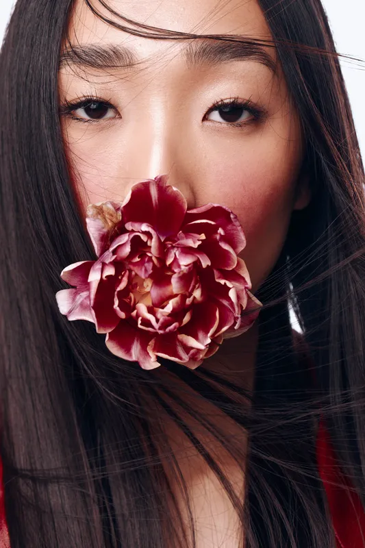 Красивая азиатская женщина с длинными чёрными волосами держит цветок перед лицом в безмятежной позе