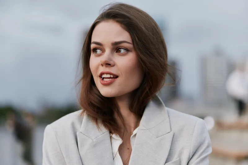 Confident businesswoman smiling outdoors against an urban backdrop, showcasing a modern, professional style and positive emotions.