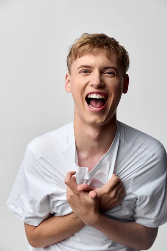 Laughing man with a bright smile, wearing a white shirt, captured in a studio setting, conveying joy, energy and casual confidence for lifestyle and advertising use