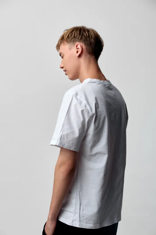 Man back white shirt casual studio pose, fashion silhouette minimalism neutral youth male wardrobe clothing simple modern clean view indoor lighting soft shadows texture fabric casualwear trend