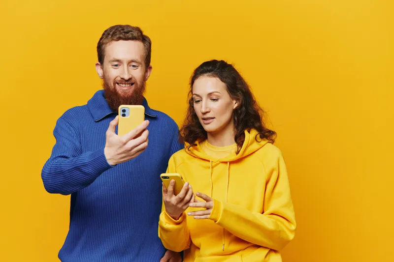 Счастливая пара — мужчина и женщина — улыбаются, держа в руках телефон и просматривая фотографии и видео в социальных сетях