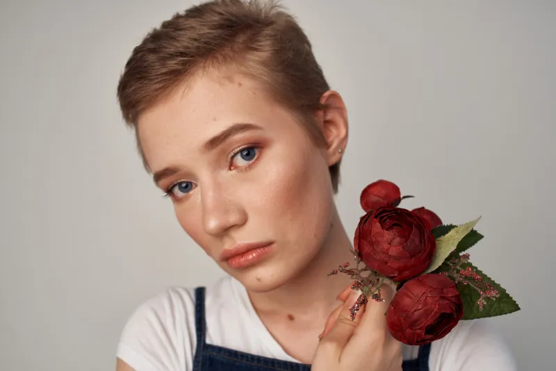 Женщина с короткой стрижкой держит цветы на светлом фоне